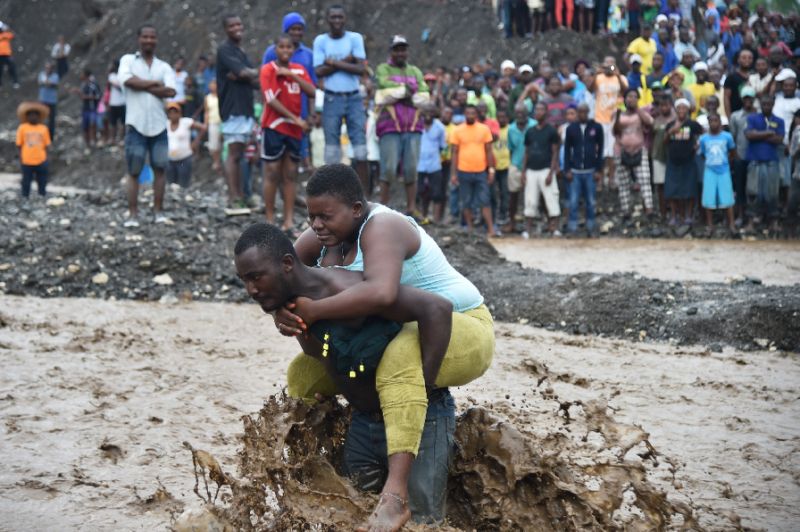 A man carries a woman across a river at Petit Goave where a bridge collapsed during the rains of the Hurricane Matthew, southwest of Port-au-Prince