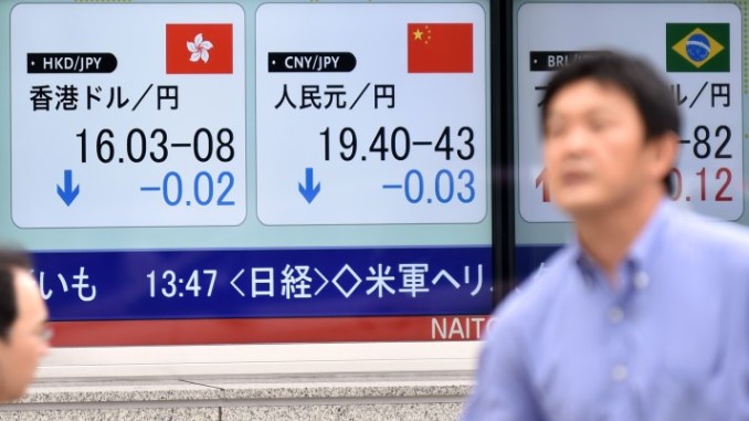 A pedestrian walks past a foreign exchange rate board, including the Chinese yuan (C) in Tokyo on August 13, 2015. Tokyo stocks closed 0.99 percent higher August 13, rallying after the previous day's losses as investors gauged the impact of China devaluing its currency for the third day in a row.   AFP PHOTO / KAZUHIRO NOGI        (Photo credit should read KAZUHIRO NOGI/AFP/Getty Images)
