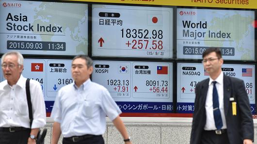 Pedestrians walk past a share price board of the Tokyo Stock Exchange in Tokyo